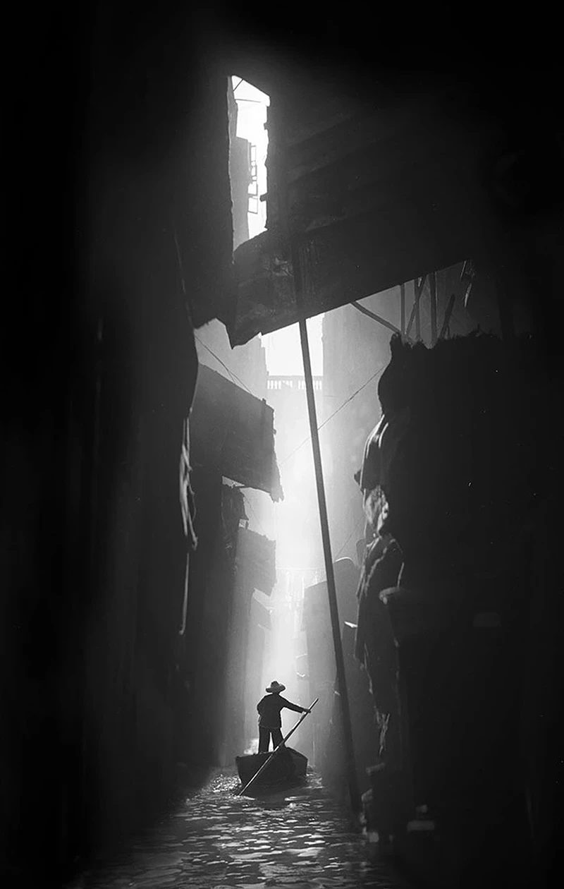 A dark, narrow alley lit by a shaft of light, in the style of Fan Ho