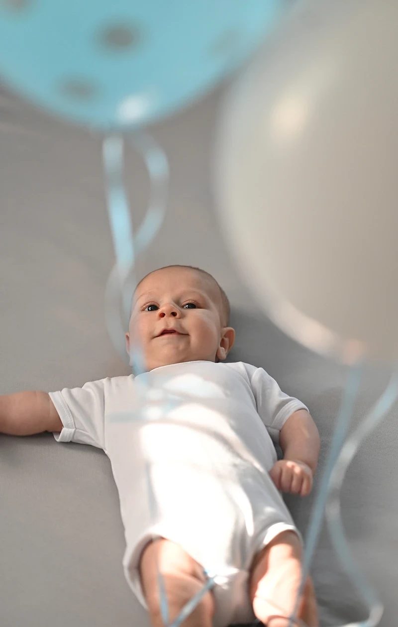 A smiling baby lying beneath balloons