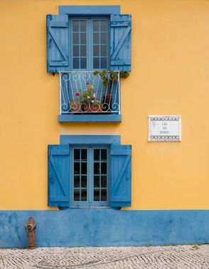 A yellow house with blue shutters and a balcony