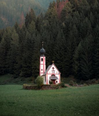 A small pink chapel in front of a dark forest